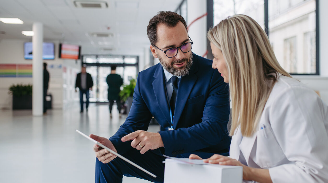 Pharmaceutical sales representative talking with doctor in clinic lobby. Ambitious male sales representative presenting new medication