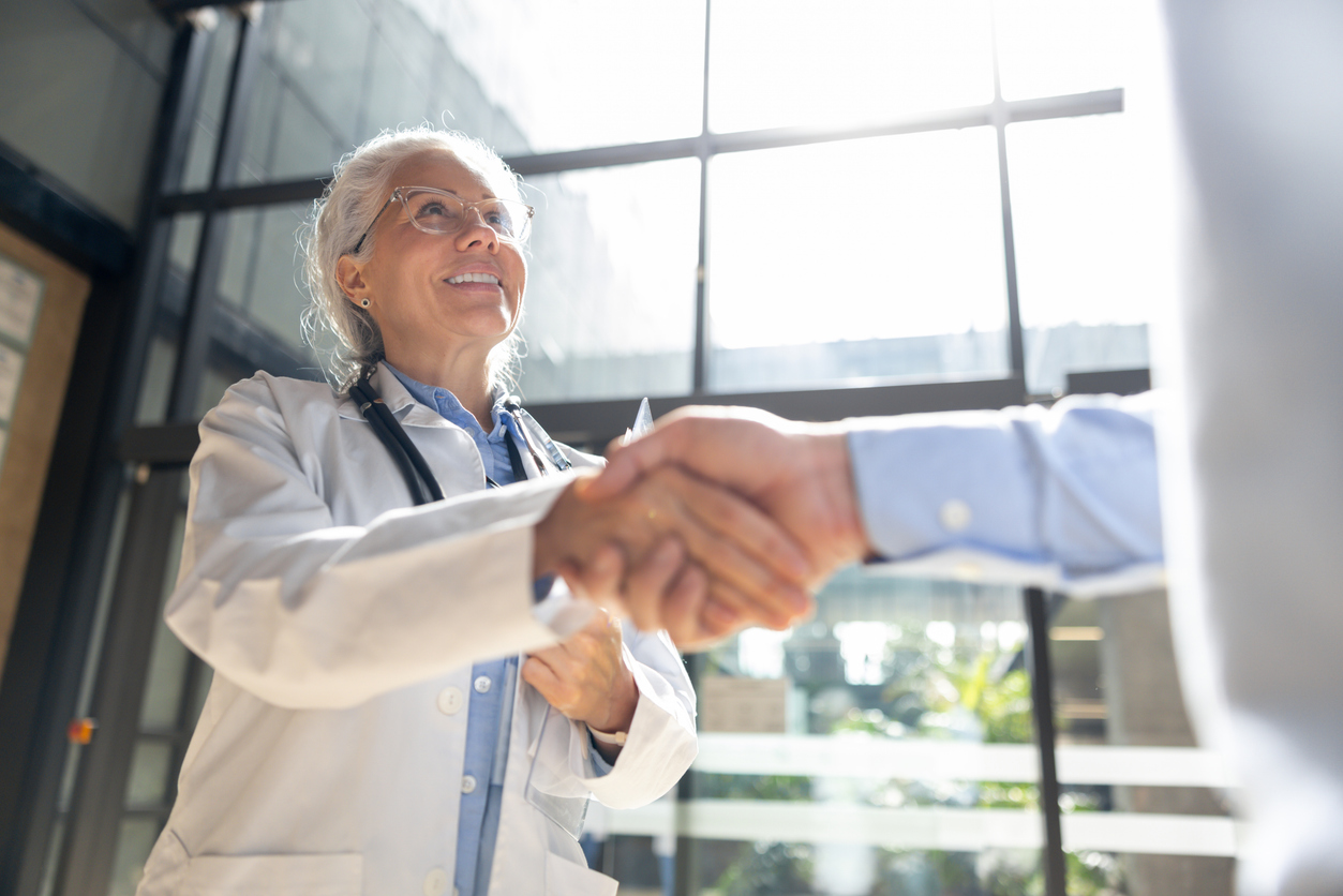 Happy doctor greeting a coworker with a handshake at the hospital