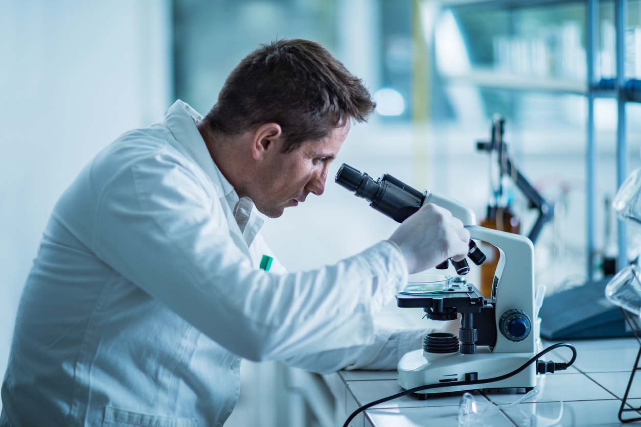 scientist sitting in a laboratory and analyzing something through a microscope